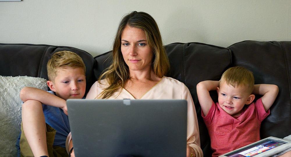 一个女人和她的两个孩子坐在沙发上玩电脑.